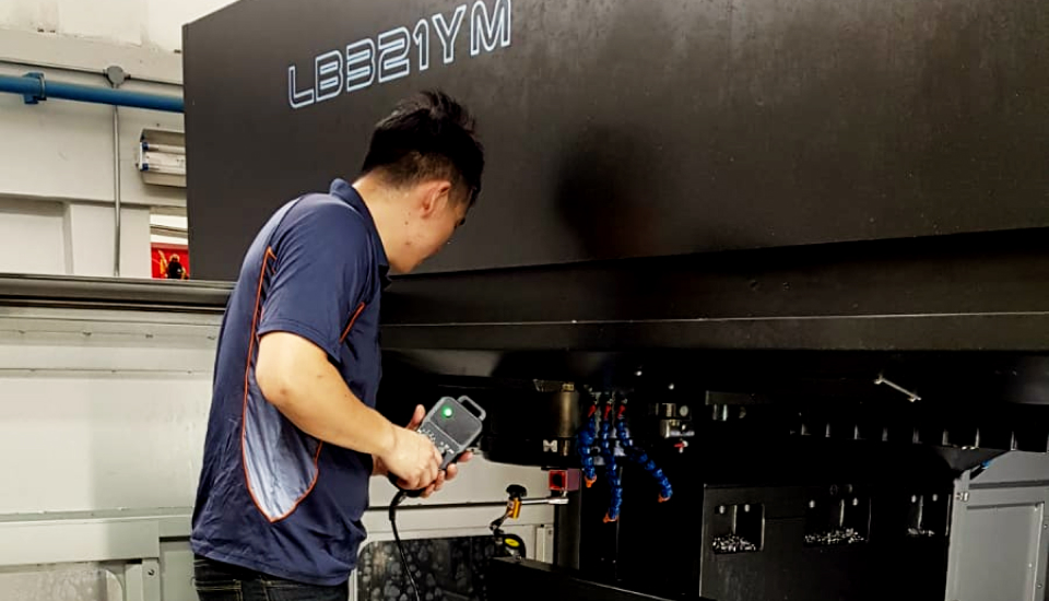 Technician operating large CNC machine model LBB21YM at Hsiu Fong Machinery, showcasing precision engineering and advanced manufacturing services in Singapore